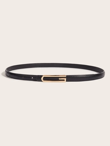 Detail of slim black leather belt with a polished golden D-shaped metal buckle on beige background