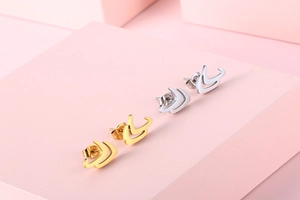 Detail of V-shaped geometric stud earrings in gold and silver on pink display cubes