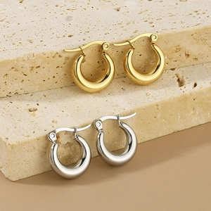 Polished gold and silver oval hoop earrings displayed on a minimalist stone pedestal