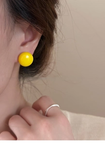 Gros plan de boucles d'oreilles rondes jaunes portées par un mannequin sur fond beige