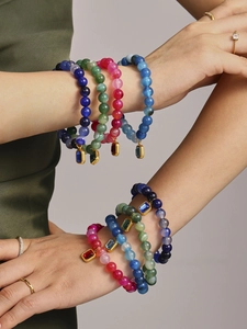 Detail of colorful beaded bracelets with gold-framed square pendants on a model arm