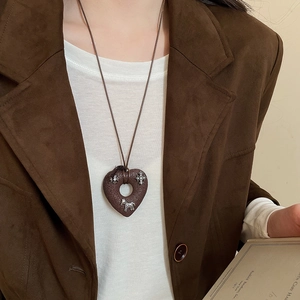 Detail of vintage heart pendant with silver horse and cross motifs on brown cord