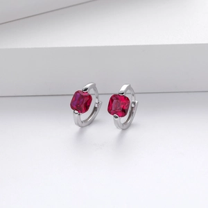 Macro shot of silver earrings with square red zircon stones on a minimalist white stand
