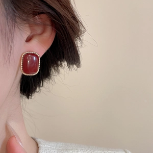 Close-up of elegant gold-tone oval earrings with red resin on woman's ear