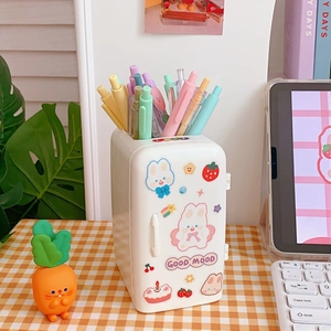 Detailed view of a white fridge-shaped pen holder with cute stickers on a checkered desk