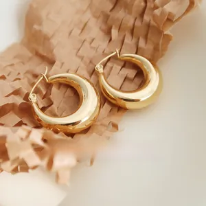 Detailed close-up of chunky gold hollow oval hoop earrings on textured honeycomb paper