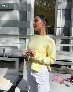 Detail of light yellow knit sweater featuring a ribbed cuff and side split hem design