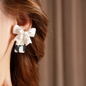 Détail de boucles d'oreilles nœud effet marbre blanc portées pour un style élégant