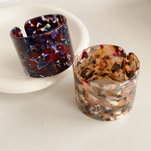 Detail view of wide open C-shape acetate bangles with dark floral and marble patterns
