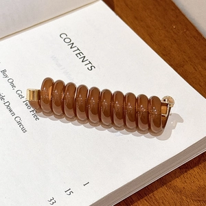 Détail d'une pince à cheveux spirale marron ambré avec des attaches dorées métalliques