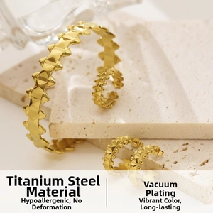 Detailed macro view of gold titanium steel rivet bangle and hoop earrings set on stone decor