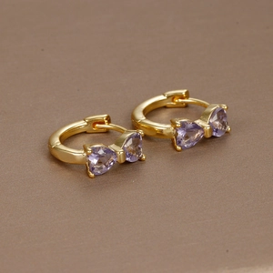 Detailed close-up of 18K gold bow earrings with purple zircon stones on a brown surface