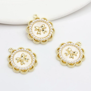 Detailed view of golden round charms with white inlay, pearls and a bow on white plate