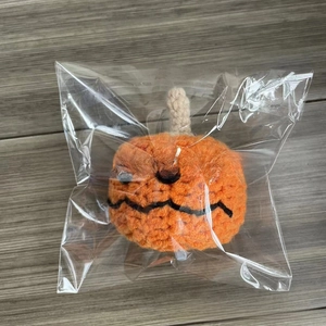 Detail of hand-knitted orange Halloween pumpkin plush in transparent protective packaging