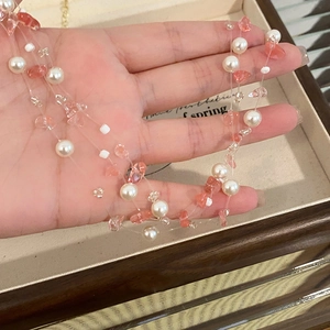 Detail of multilayer necklace featuring white pearls and pink crystal stones held by hand