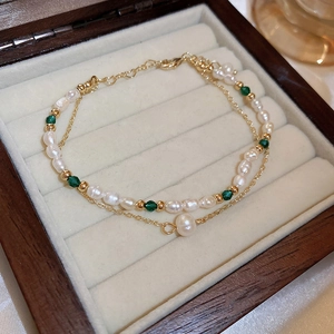 Close-up of double-layer bracelet with baroque pearls, green beads and gold tassels