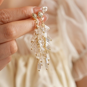 Detail of long gold earrings with crystal beads and stars held by hand on beige cloth