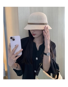 Dettaglio cappello a secchiello intrecciato beige con cinturino in pelle marrone e fibbia d'oro