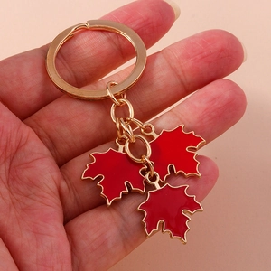 Detail of red maple leaf keychain with golden metal ring and polished enamel charms