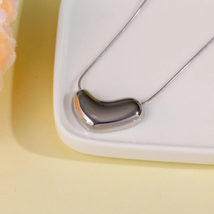 Detail of polished silver heart pendant on a sleek snake chain over a white ceramic tray