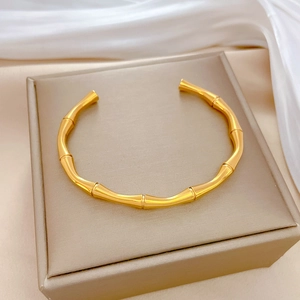 Minimalist bamboo-style gold titanium steel open bangle displayed on a luxury jewelry box