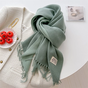 Detail of green cashmere-feel scarf with fringe and logo tag on a white jacket