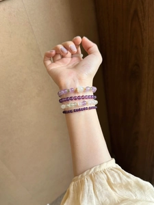 Detailed view of stacked amethyst and green stone beaded bracelets on a wrist