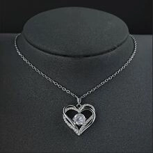 Close-up of silver heart pendant necklace with clear gemstones on black mannequin