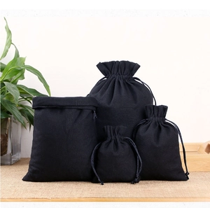 Set of four black drawstring canvas jewelry pouches in various sizes on a wooden tray