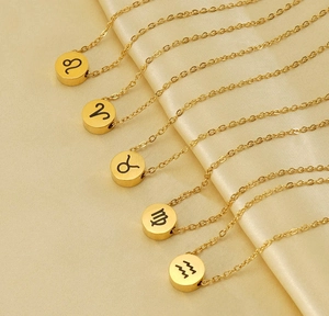 Dettaglio di collane zodiacali dorate con simboli incisi su sfondo di seta color champagne