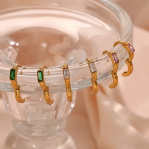 Détail de créoles dorées avec zircons rectangulaires en vert, blanc transparent et rose