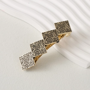 Close-up of gold hair clip featuring five square pieces with geometric line textures