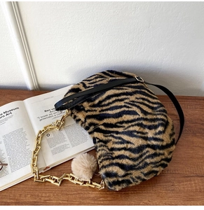 Detail of tiger print plush tote bag with gold chain strap and beige pompom charm