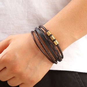 Close-up of layered brown braided leather bracelet with gold metal rings on male wrist