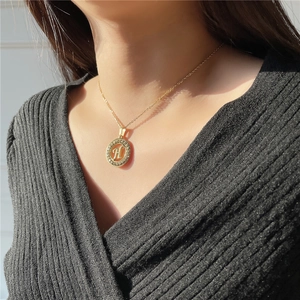 Detail of gold initial necklace with crystal-encrusted letter H on a round pendant
