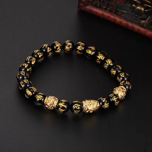 Gros plan de perles d'onyx noir avec gravure de mantra doré et breloque tête de Bouddha