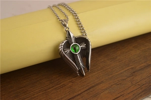 Détail macro d'un collier croix vintage en argent avec œil-de-chat vert et ailes d'ange