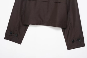 Detail eines dunkelbraunen Trenchcoats mit Harzknöpfen sowie Saum und Manschetten aus Webstoff