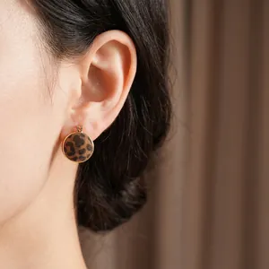 Flocked leopard print round stud earrings with gold metal trim worn by a model