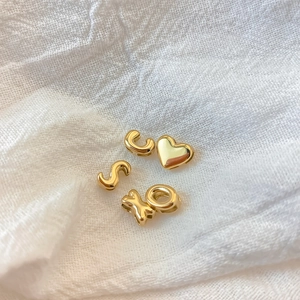 Close-up of golden alphabet letters S, C, X, O and heart bead charms on white textured fabric