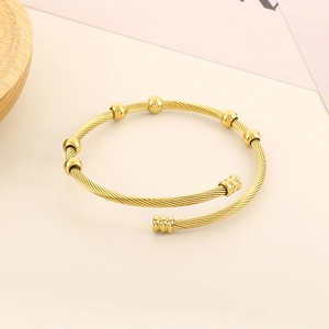 Macro detail of golden cable wire open bangle featuring five polished beads and screw ends