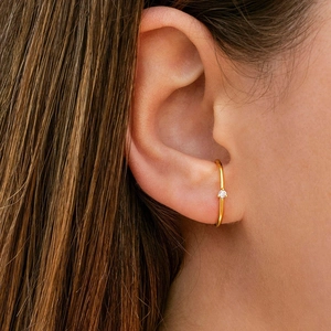 Elegant gold cuff earring with a single sparkling diamond worn by a model in a close-up view
