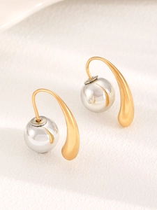 Close-up of gold and silver teardrop hook earrings with polished metallic sphere pendants