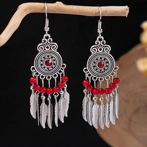 Detail of bohemian red fringe earrings hanging on a branch with a dark background