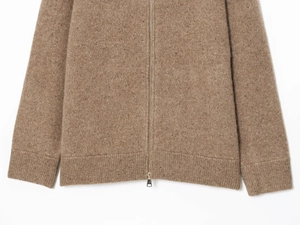 Dettaglio del cardigan in maglia marrone con zip metallica e polsini ampi a costine