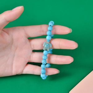 Detail of turquoise beaded turtle bracelet on wrist with bright green background