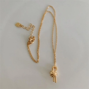 Detailed view of gold knot pendant necklace with heart-shaped tail charm and fine chain