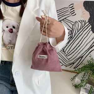 Minimalist pink corduroy drawstring storage bag with woven label held by hand