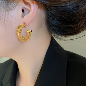 Detail of twisted C-shaped gold earring on model showing spiral metallic texture