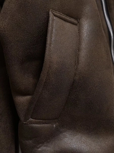 Detail of dark brown leather jacket featuring a side pocket and smooth metal zipper texture